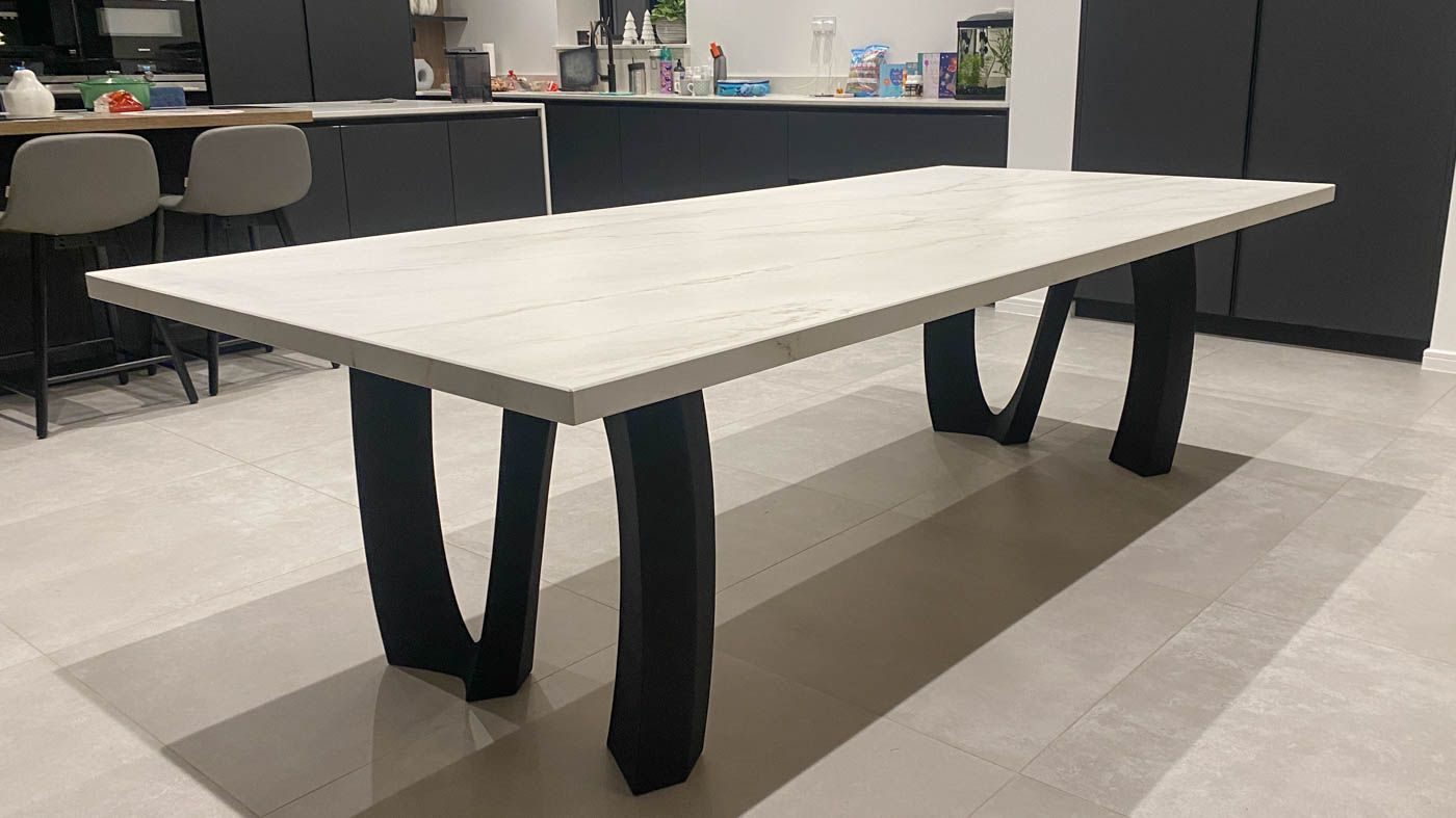 A white Dekton dining table on a black steel curved base in a kitchen